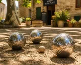 Close-up of shiny pétanque balls on a sunlit clay court under the shade of plane trees in a Provençal village setting.